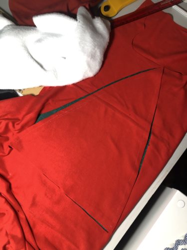 roter Jersey liegt ausgebreitet auf dem Tisch, ein dreieckiges Stück ist bereits ausgeschnitten. 