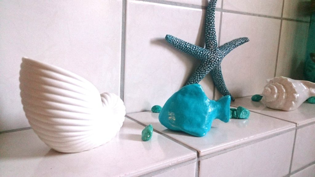 Selbstgebastelter Fisch aus Fimo in karibischem ozeanblau als Deko zwischen Muscheln und Seestern