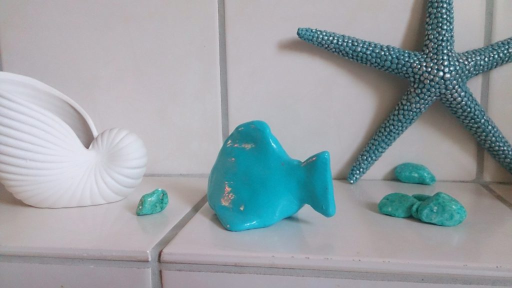 Selbstgebastelter Fisch aus Fimo in karibischem ozeanblau als Deko zwischen Muscheln und Seestern