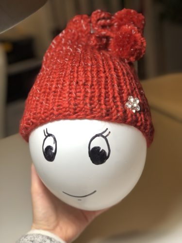 Die Loopmütze sitzt als Mütze auf einem weißen Luftballon anstelle eines Kinderkopfes. Dem Luftballon wurde ein freundliches Gesicht aufgemalt.