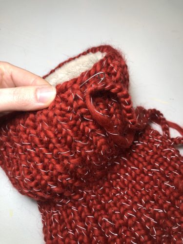 Die Luftmaschenkette wird mit einer Sicherheitsnadel durch den Strickloop in den Tunnel eingeführt.