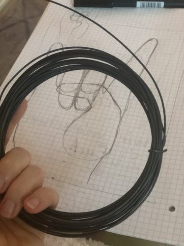 Im Hintergrund liegt die Zeichnung auf Karopapier, im Vordergrund hält verschiedenArt die schwarze Drahtrolle ins Bild