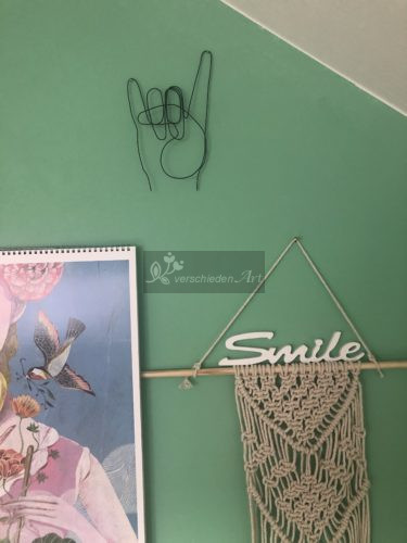 Nochmal die Metal Hand aus schwarzem Stahldraht an der grünen Wand.
