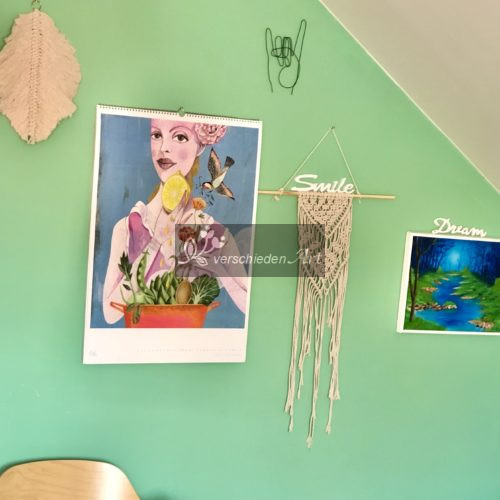 Metal Hand aus schwarzem Stahldraht hängt an der grün gestrichenen Wand. Man sieht noch einen Kalender und ein Makrame daneben